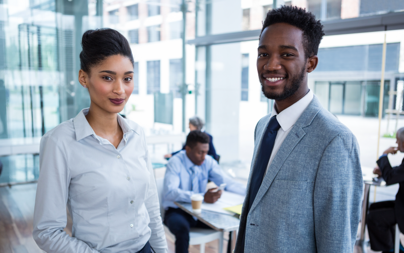A imagem mostra um homem e uma mulher conversando em pé na sala da empresa. Ela representa como realizar contratação para cargos de liderança.