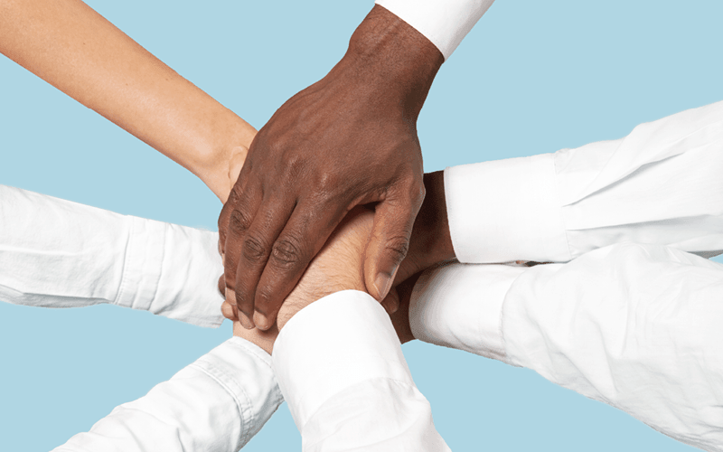 A imagem mostra várias mãos unidas ao centro, uma sobre a outra. Ela busca representar a união de equipes e retenção de talentos, o que contribui para redução do turnover.