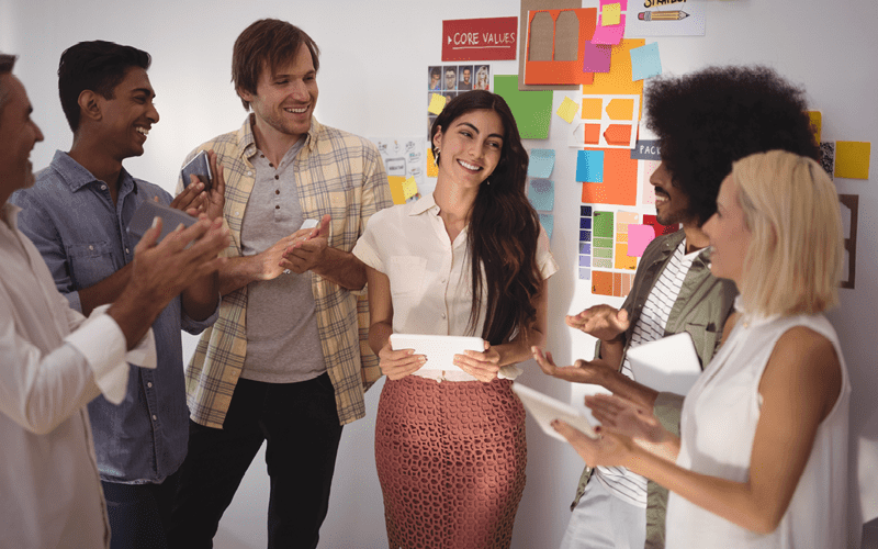 A imagem mostra alguns jovens adultos conversando felizes, eles estão em frente a um mural de anotações. A imagem busca representar as características dos millennials.