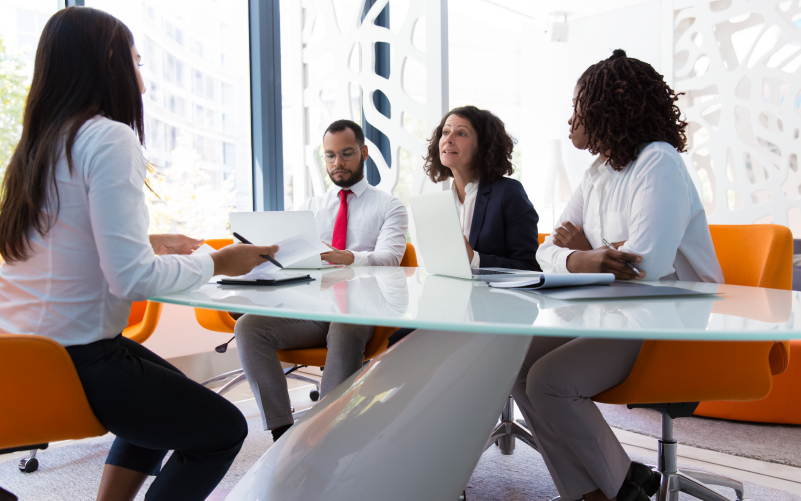 A imagem mostra alguns colegas de equipe sentados ao redor de uma mesa conversando. Ela busca representar, de forma lúdica, como selecionar o candidato certo para a sua empresa.