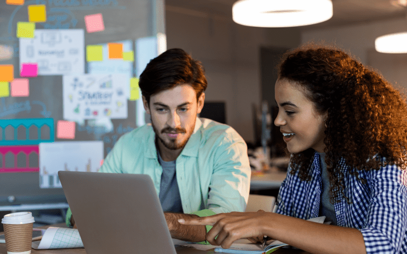 A imagem mostra um homem e uma mulher mexendo em um notebook, em um ambiente descontraído de trabalho. A foto representa, de forma lúdica, pessoas pesquisando por um assunto na internet (como a teoria dos traços de personalidade, foco do post que está sendo apresentado).