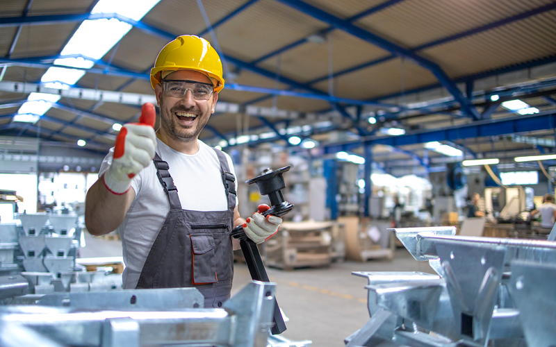 Funcionário temporário de fábrica sorrindo e realizando gesto de felicidade com as mãos. A imagem representa os benefícios e oportunidades do trabalho temporário.