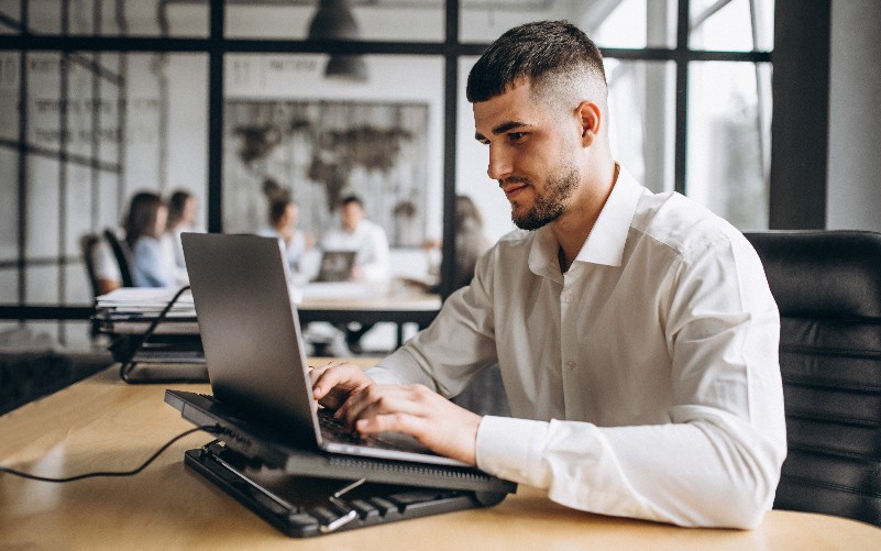 A imagem mostra um rapaz com roupas sociais digitando em seu notebook. A imagem busca representar o uso de People Analytics para recrutamento e seleção.