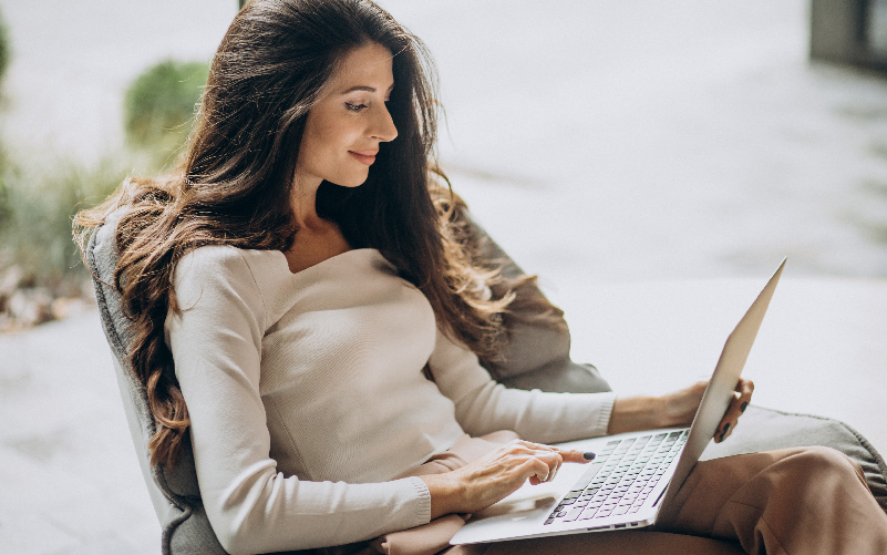 A imagem mostra uma mulher jovem sentada confortavelmente e com um computador no colo. Ela busca demonstrar, de forma lúdica, como funcionam as análises e testes para recrutamento preditivo.