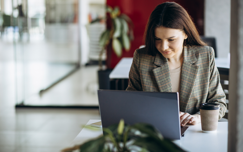 Imagem e mulher sentada mexendo em um notebook. Ela usa roupa sociais e está em um ambiente de escritório. O objetivo da imagem é representar o planejamento e execução de um projeto de recrutamento Belo Horizonte.