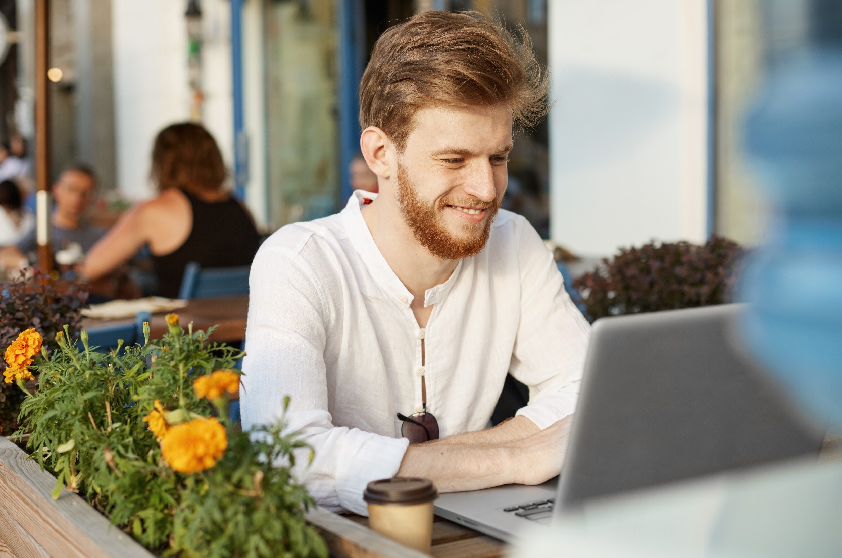 Na imagem, vemos um homem sentado ao ar livre e utilizando um notebook. Ele está sorrindo e otimista ao pesquisar sobre o cenário do trabalho temporário no Brasil.