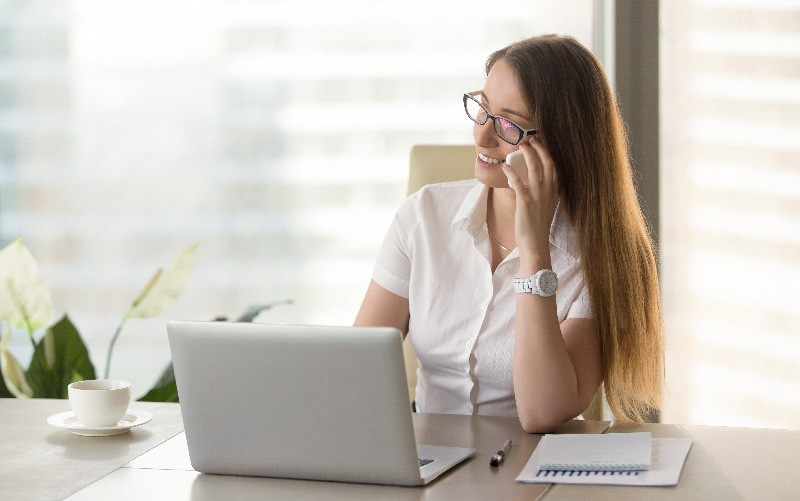 A imagem mostra uma jovem sorrindo enquanto usa o computador. A imagem representa a importância do retorno em processos seletivos.