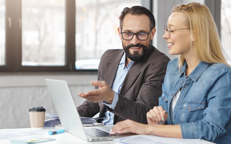 Na imagem, podemos ver um homem e uma mulher conversando. Ambos estão sentados em uma mesa, com um notebook no centro. Eles falam sobre os termos corretos para se referir a trabalho temporário.