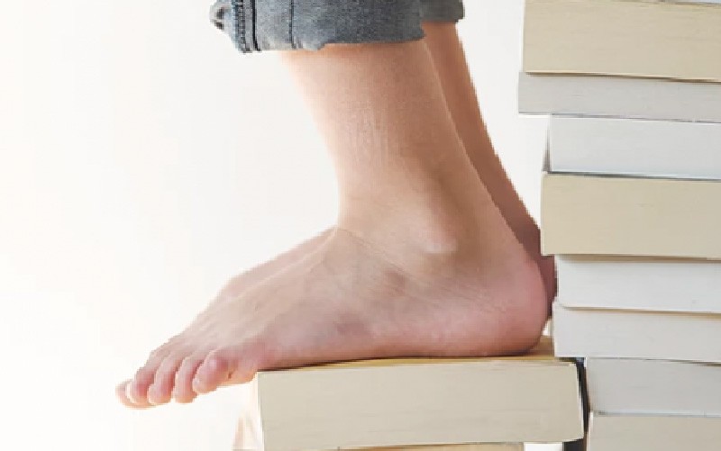A imagem mostra os pés de uma pessoa sobre uma pilha de livros, simbolizando os degraus do aprendizado e processo de sempre reaprender que é proposto no conceito de reskilling.