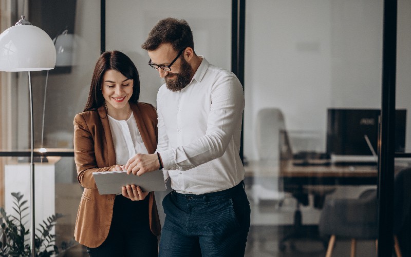 A imagem mostra um homem e uma mulher conversando e analisando um documento. A imagem busca representar a criação e análise do job description para uma vaga de emprego.