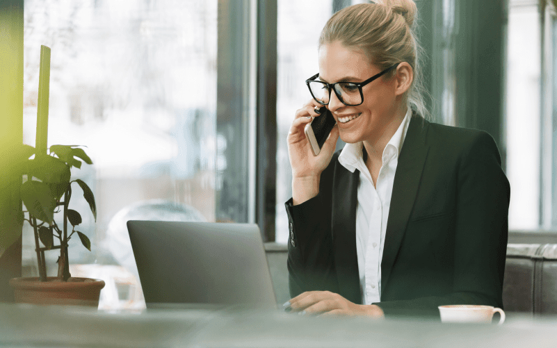 Ao centro da imagem vemos uma mulher no ambiente de trabalho e utilizando roupas sociais. Ela sorri enquanto fala ao telefone e observa a tela do computador. A imagem busca representar, de forma lúdica, a troce de feedback positivo e negativo entre equipes.