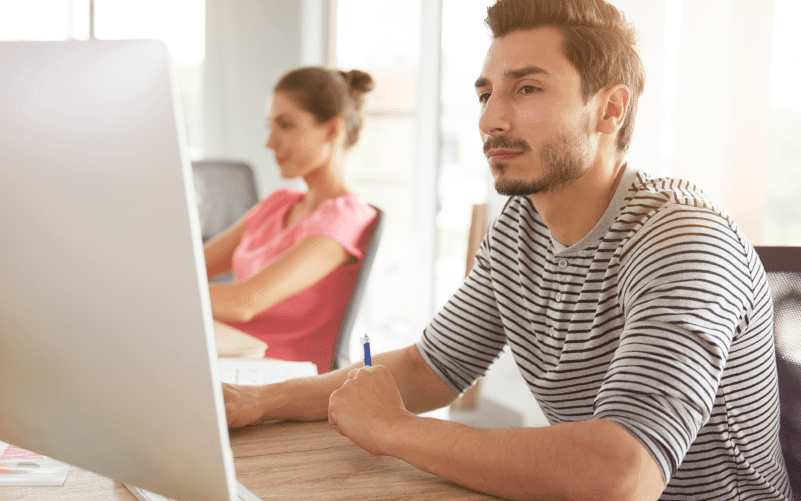 A imagem mostra um homem e uma mulher usando o computador, com destaque no rapaz, que está mais perto da câmera. A imagem busca representar o que é RH digital e suas vantagens.