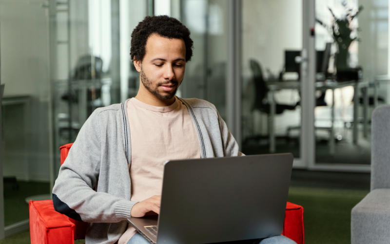 Homem sentado em poltrona com um notebook no colo, aparentemente ele está realizando pesquisas sobre como contratar trabalhadores temporários.