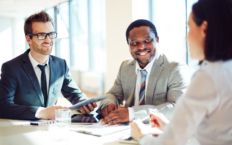 A imagem mostra três profissionais sentados ao redor de uma mesa conversando. Ela busca representar o que é recrutamento inteligente.