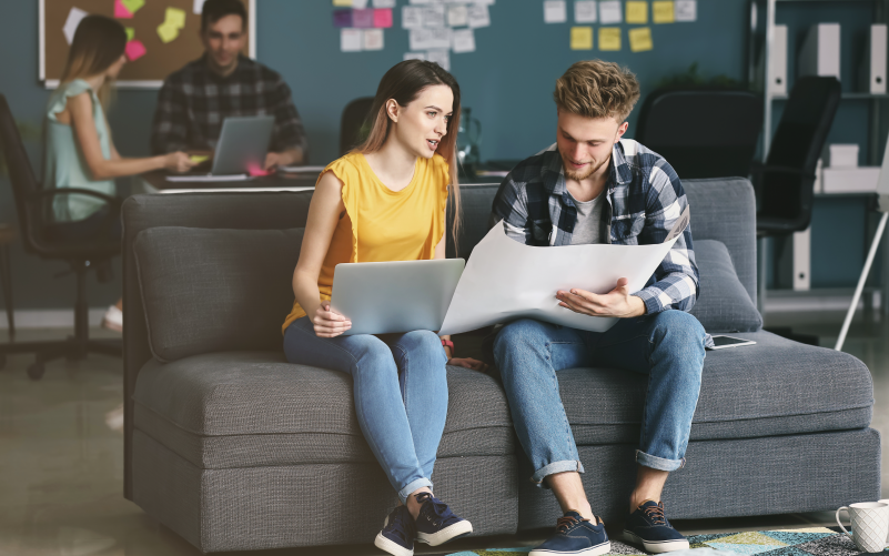 A imagem mostra um homem e uma mulher jovens conversando sobre como implementar um programa de desenvolvimento para estagiários e trainees na empresa onde trabalham.