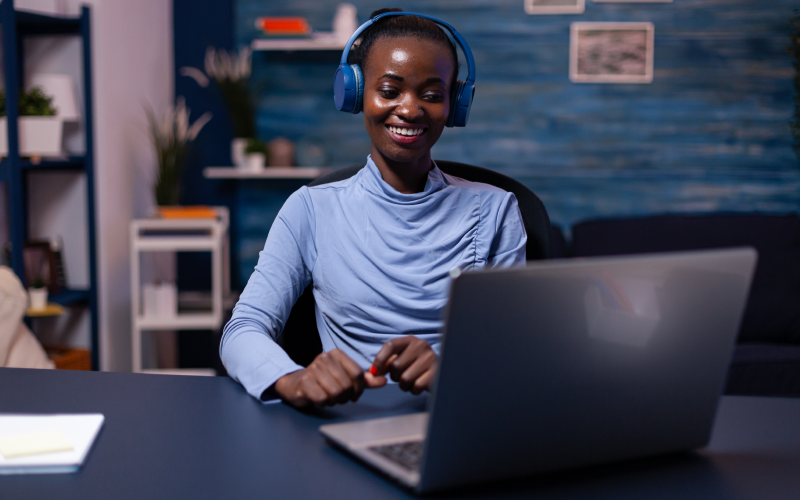 A imagem mostra uma mulher negra mexendo em um notebook. Ela está sorrindo enquanto pesquisa mais sobre as melhores ferramentas para gestão de pessoas e processos. A cor predominante da imagem é azul, que também é refletido nas roupas que ela está usando e na própria decoração da sala em que a mulher está.