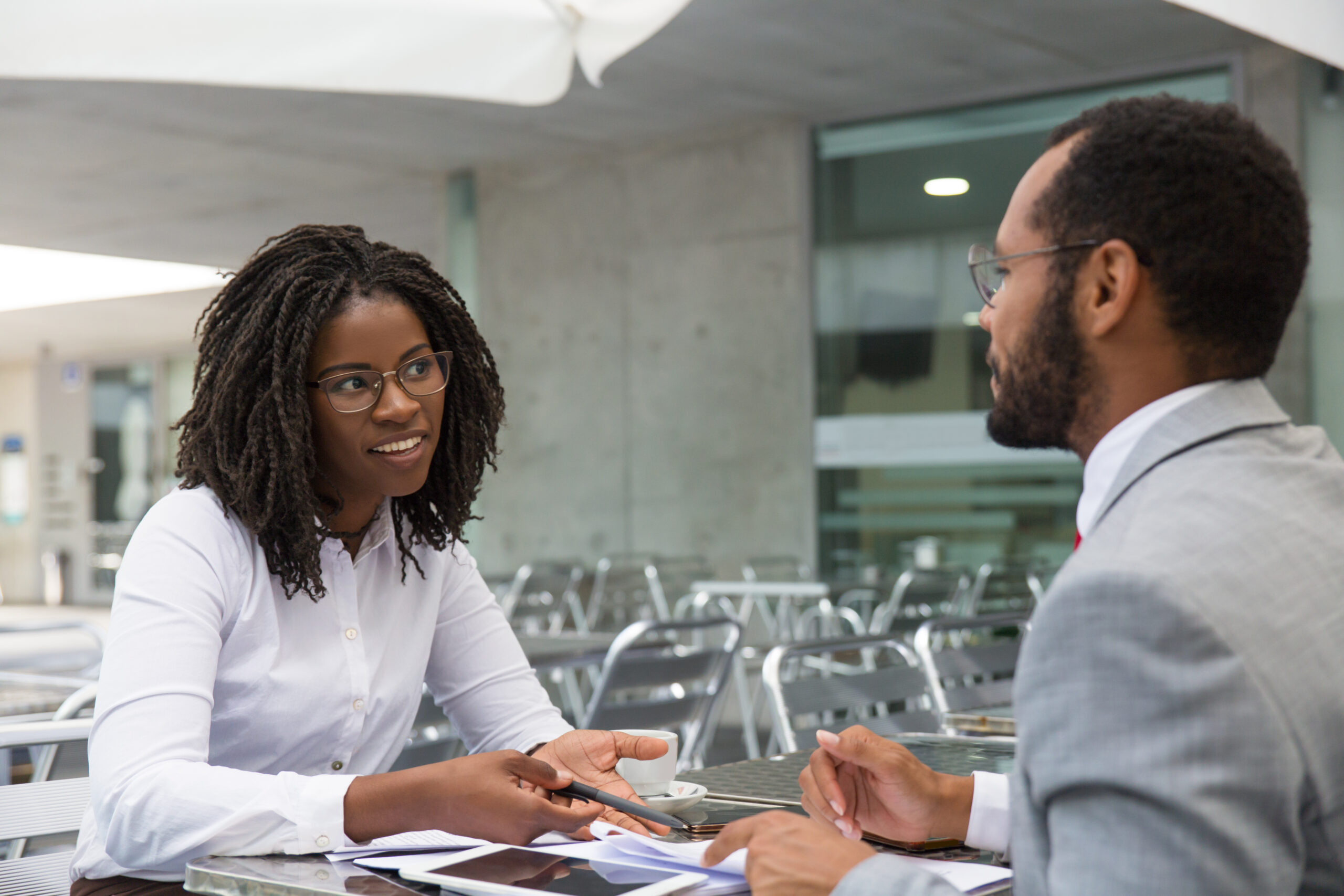 A imagem mostra duas pessoas, sendo um homem e uma mulher, com roupas sociais sentados frente a frente em uma mesa de escritório. A imagem busca representar de forma lúdica uma das etapas do processo de recrutamento e seleção.