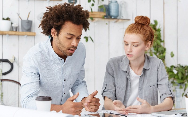 A imagem mostra um homem negro e uma mulher branca conversando sobre linguagem neutra e linguagem inclusiva.