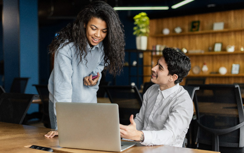 A imagem mostra uma mulher negra e um homem branco conversando em um ambiente de trabalho informal. Eles discutem sobre como será feita a fiscalização da LGPD (Lei Geral de Proteção de Dados) em 2022.