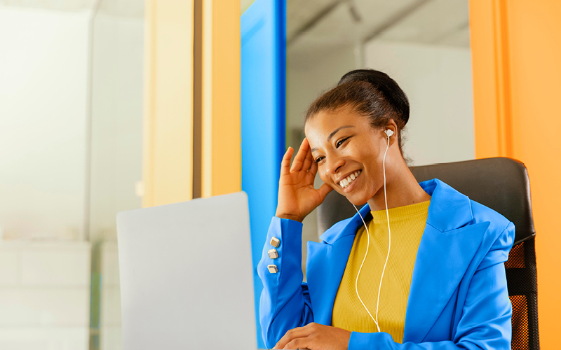 Mulher negra sorrindo enquanto trabalha em um notebook. Ela está lendo um conteúdo que aborda o desenvolvimento de líderes e carreiras.