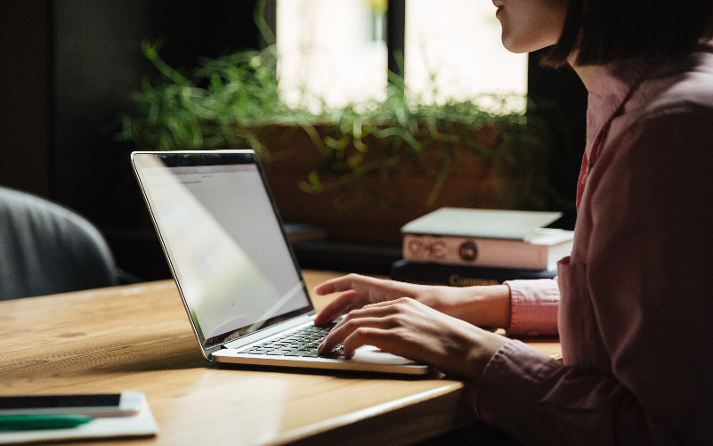 Mulher trabalhando em uma mesa com seu notebook. Ela está analisando como usar o ATS no recrutamento e seleção da empresa onde trabalha.