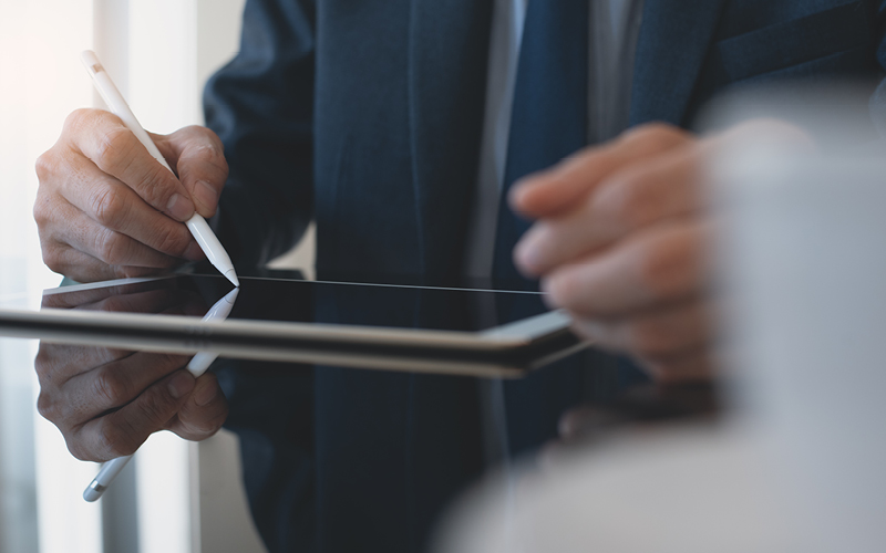 Mão masculina mexendo em um tablet. A imagem busca retratar a avaliação de um candidato por meio do recrutamento às cegas, realizado com o apoio da tecnologia no RH.