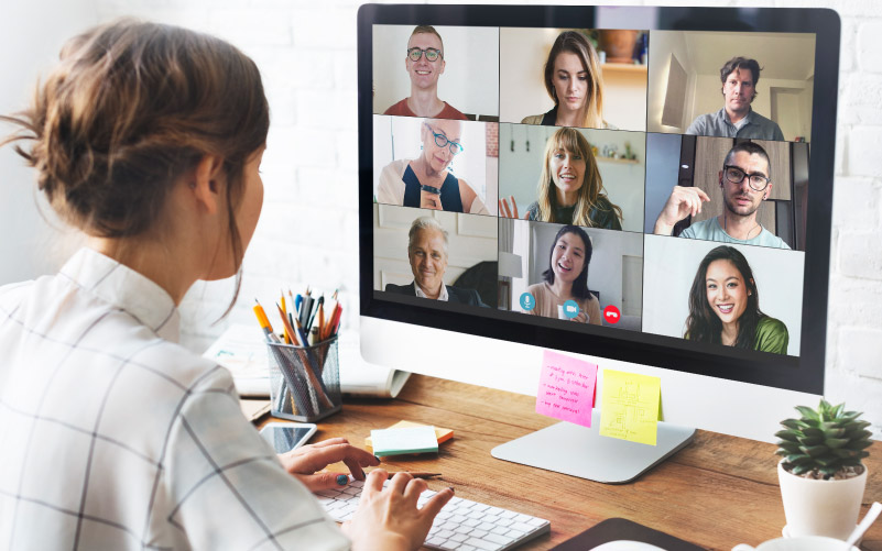 Mulher em reunião online. Na tela do seu computador, ela vê as outras pessoas do seu time. A imagem busca retratar o alinhamento necessário para gerenciar uma equipe remota.