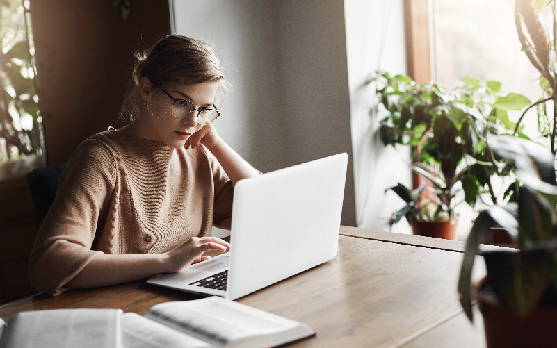 Mulher estudando em um notebook sobre os principais direitos do estagiário. Ela trabalha na área de recursos humanos e precisa desenvolver um novo programa de estágio na empresa em que atua.