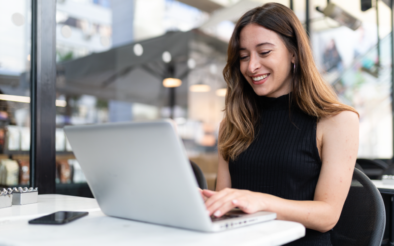 Jovem profissional trabalhando. Ela está sorrindo e parece estar tranquila realizando suas atividades, pois entende a importância de cuidar da saúde mental no trabalho.