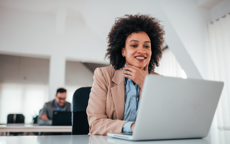 Mulher negra em um escritório. Ela está mexendo em um notebook, pesquisando sobre tecnologia cognitiva no rh para entender como funciona na prática.