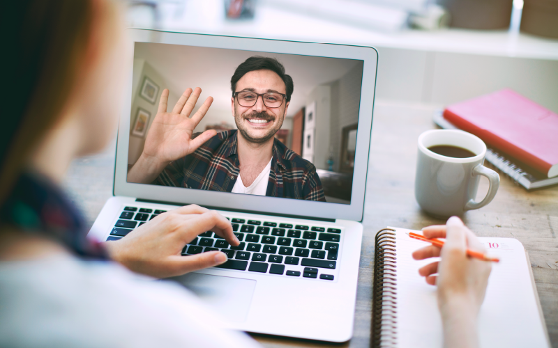 Imagem com pessoa desfocada em uma chamada de vídeo no computador. O destaque está na tela, que representa uma etapa do recrutamento online.