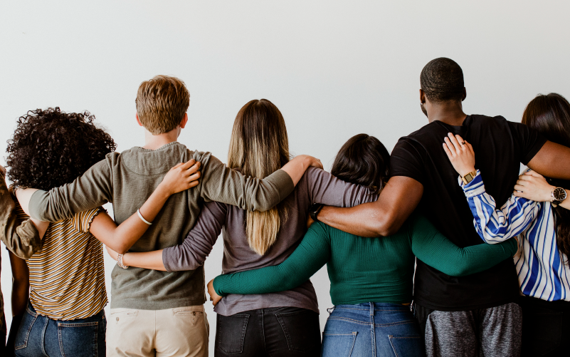 Grupo de pessoas abraçadas, lado a lado, de costas. A imagem busca representar a união de pessoas durante o Setembro Amarelo, mostrando a importância das redes de apoio.