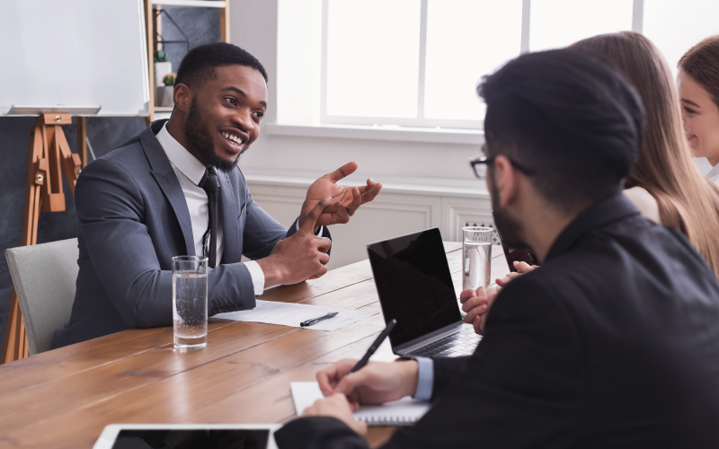 Funcionários homens e mulheres sentados em uma mesa de um escritório representando uma entrevista comportamental