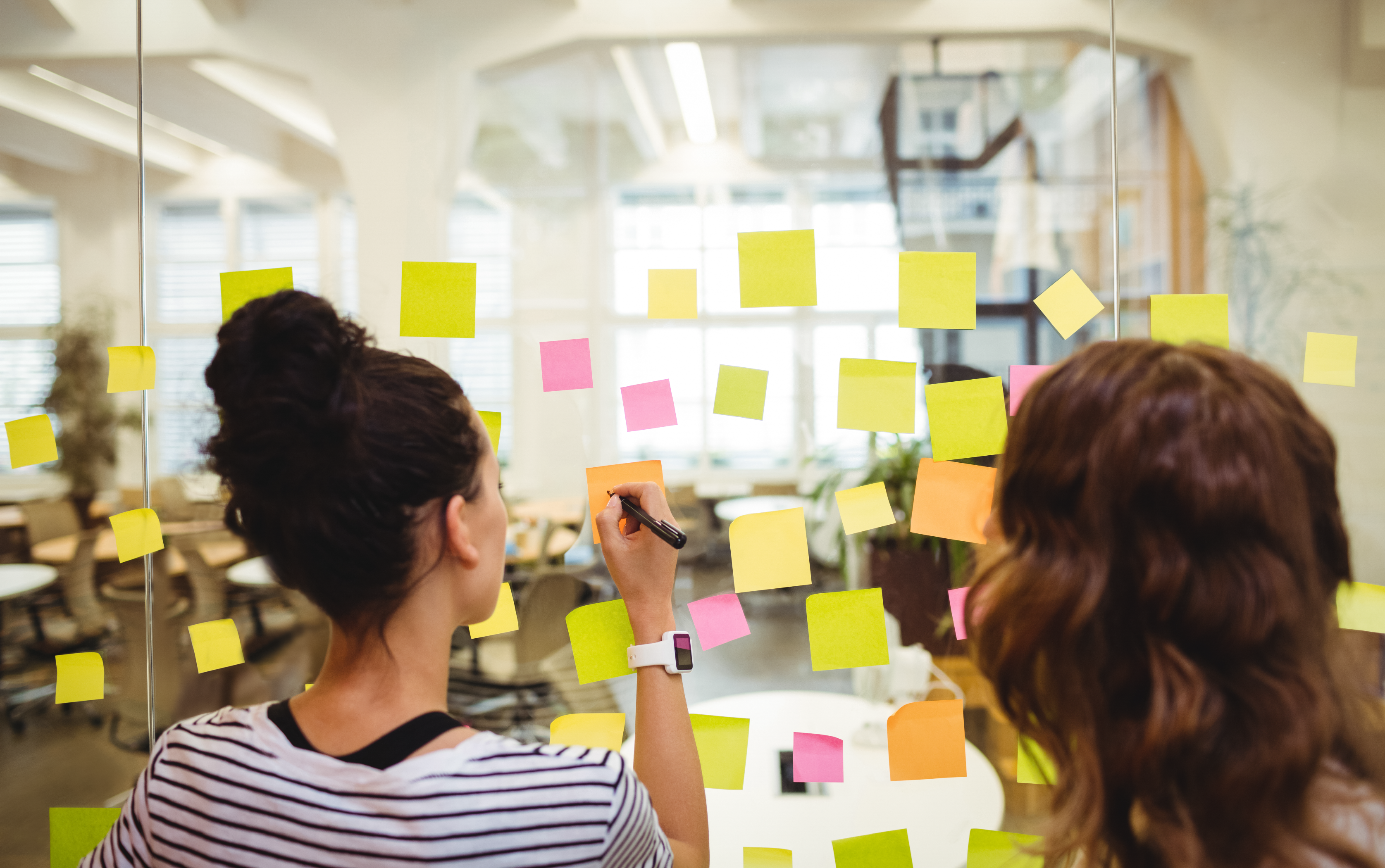 Duas mulheres escrevendo em blocos de notas coloridos representando a metodologia sprint em uma empresa