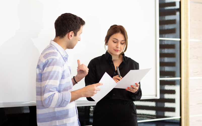 Imagem de capa para blog sobre avaliação 360 nas empresas. Na foto, um homem e uma mulher conversando e analisando avaliações de funcionários.