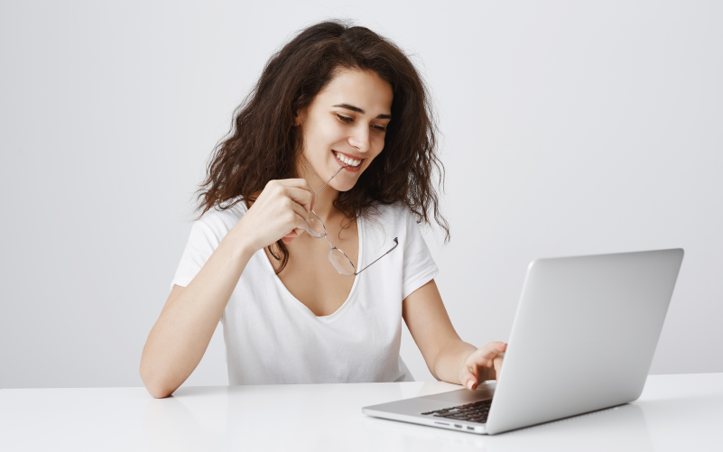Mulher branca olhando para o computador e sorrindo, para simular uma consultoria de gestão de pessoas