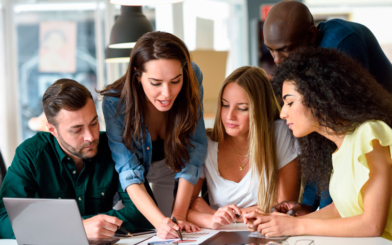 Imagem de capa de post blog sobre treinamento de estagiários. Na foto, observamos um grupo de pessoas conversando e analisando papeis, como se fosse uma dinâmica de treinamento.