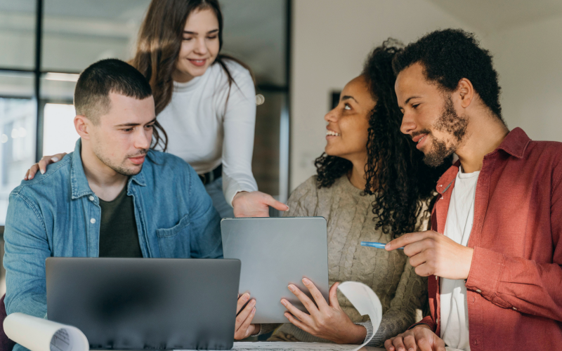 Imagem de capa de post blog sobre avaliação por competências. Na foto, observa-se um grupo diverso de quatro pessoas jovens, sendo duas mulheres e dois homens.