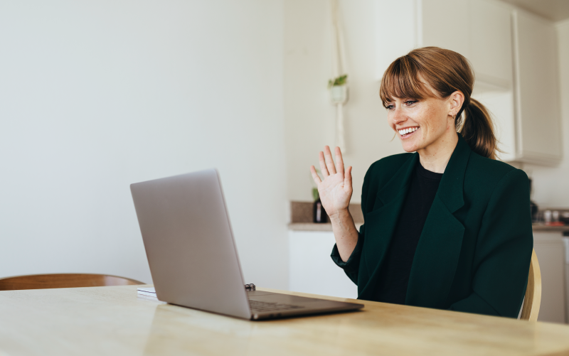 Imagem de capa de post blog sobre contratação remota. Na foto, observa-se uma mulher jovem sorrindo e acenando para alguém que aparece na tela de um notebook, simulando uma entrevista remota.