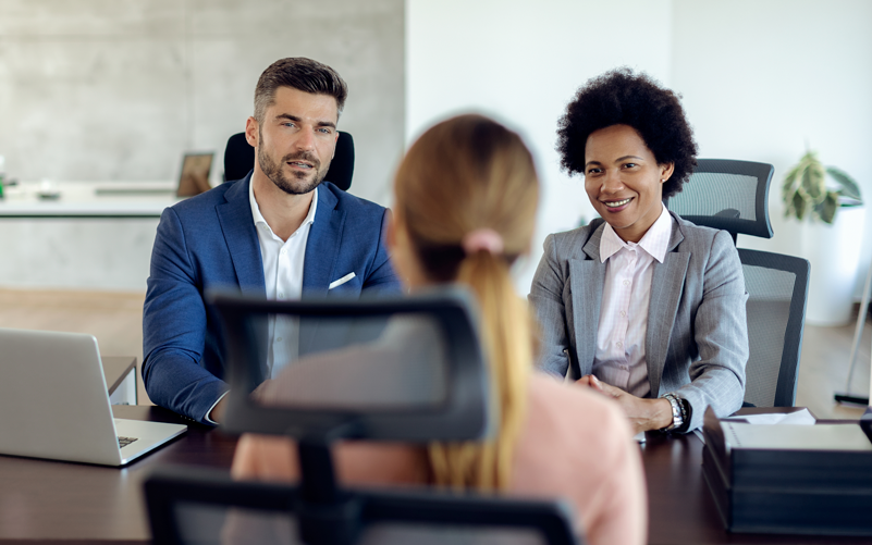 Imagem de capa de post blog sobre recrutamento de executivos. Na foto, há três pessoas. Duas delas estão entrevistando uma profissional em potencial para ocupar um cargo de liderança na empresa.