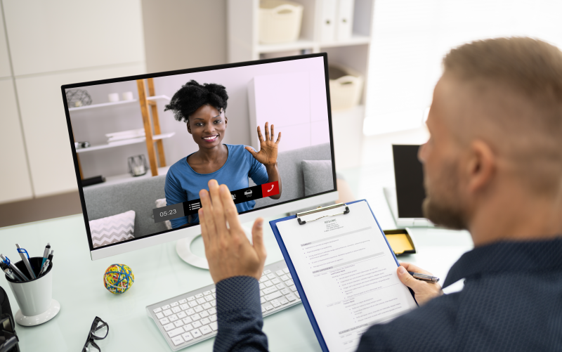 Imagem de capa de post blog ilustrando um conteúdo sobre roteiro de entrevista. Na foto, um homem conversa e acena para uma mulher por meio de uma videoconferência, simulando o início de uma entrevista de emprego online.