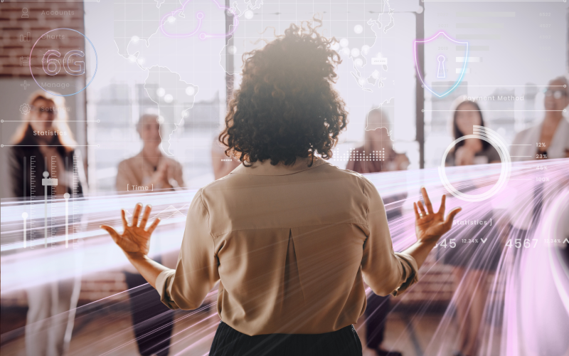 Profissional de costas reunida com um grupo, diante de gráficos digitais e elementos tecnológicos que representam análise de competências, uso de dados e processos de contratação e desenvolvimento baseados em habilidades.